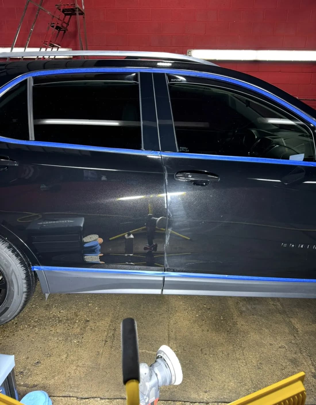 Black SUV masked with tape mid paint-correction, polisher in the foreground
